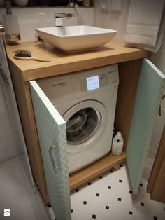 a washer sitting inside of a wooden cabinet next to a bowl on top of a sink