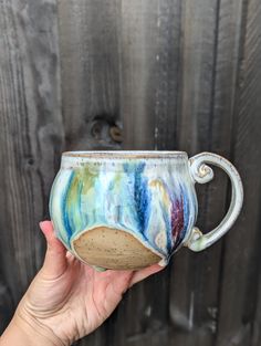 a hand holding a ceramic mug with colorful designs on it's side and inside