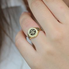 a close up of a person's hand wearing a gold ring with an emblem on it