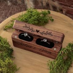 two wedding rings sitting in a wooden box on top of mossy branches and leaves