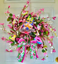 a welcome wreath with flamingos and flowers hanging on the front door to someone's house