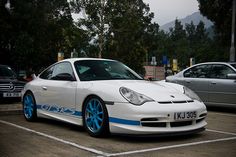 a white car with blue rims parked in a parking lot next to other cars