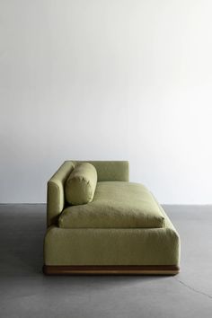 a green couch sitting on top of a cement floor next to a white wall in an empty room