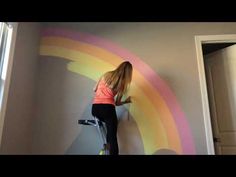 a woman painting a rainbow wall in her home