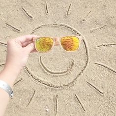 someone is holding their sunglasses in front of the sun drawing on the sand with them