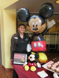 a woman standing in front of a table with mickey mouse balloons and cupcakes