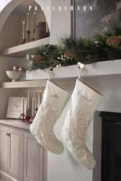 two christmas stockings hanging from a mantel with candles and pine cones on the mantle