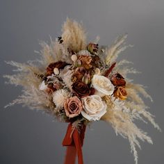 a bridal bouquet with dried flowers and feathers on display in front of a gray background