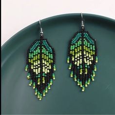 a pair of green and black beaded earrings sitting on top of a blue plate