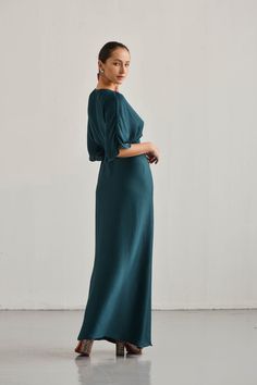 a woman in a long green dress standing with her hands on her hips and looking off to the side