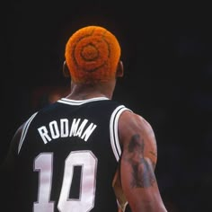 the back of a basketball player with an orange mohawk on his head and tattoos on his arm