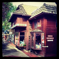 a row of wooden buildings sitting next to each other on a side walk in front of trees