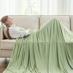 a woman laying on top of a couch covered in a blanket