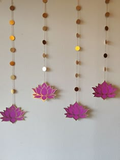 three paper lotuses hanging from strings on a wall with circles and beads around them