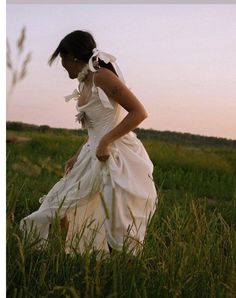 a woman in a white dress walking through tall grass