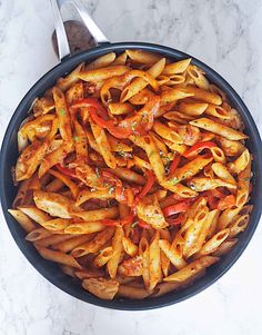 a pan filled with pasta and sauce on top of a white marble countertop next to a spoon