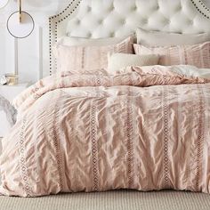 a bed with pink comforter and pillows in a bedroom next to a white headboard