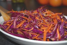 a bowl full of red cabbage and carrots with a wooden spoon in the bowl