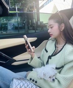 a woman sitting in the back seat of a car holding a cell phone and a small white dog