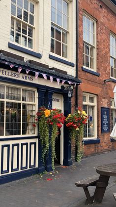 the outside of a building with flowers hanging from it's windows and tables in front