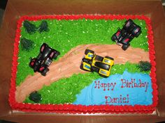 a birthday cake decorated with racing cars on a dirt track in the grass and trees