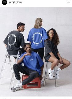 four people sitting on stools in front of a wall wearing sweatshirts and sweatpants