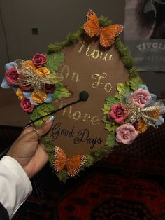 a person holding a graduation cap decorated with flowers and butterflies that says, mom on to more good days