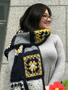 a woman is wearing a scarf with flowers on it and smiling while standing next to a stone wall