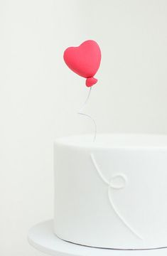 a white cake with a red heart balloon on top