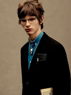 a young man wearing glasses and a blue shirt is standing in front of a wall