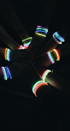 several people are holding their hands together with glowing bracelets