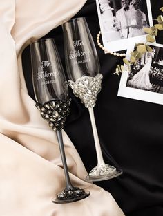 two wine glasses sitting next to each other on top of a black cloth covered bed