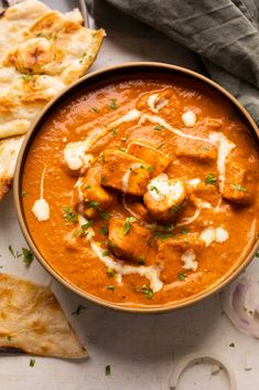 a bowl filled with red curry next to pita bread