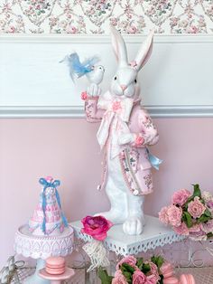 a white rabbit statue sitting on top of a table next to pink flowers and cakes