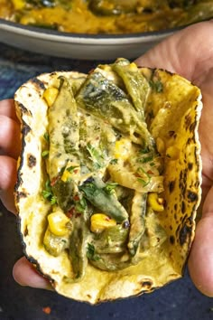 a hand holding a tortilla filled with green beans, corn and cheese sauce