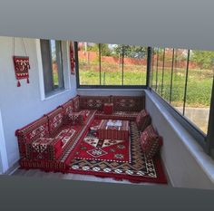 a red couch sitting in front of a window on top of a rug covered floor