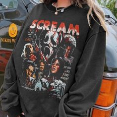 a woman standing next to a car wearing a sweatshirt with the words scream on it