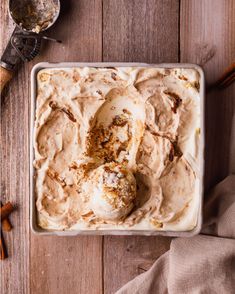 a bowl filled with ice cream next to two spoons and cinnamon sticks on a wooden table