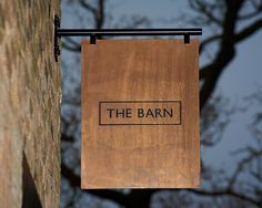 a wooden sign hanging from the side of a brick building next to a tall tree