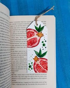 an open book with a paper tag on top of it that has pomegranates and leaves