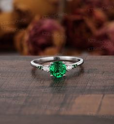 a ring with a green stone and three white stones on it sitting on a table