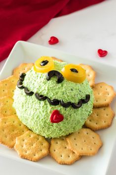 there is a green cake with eyes on it and crackers in the shape of hearts