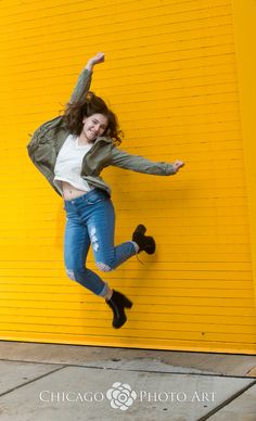 a young woman jumping in the air with her arms outstretched and legs spread out, against a yellow wall