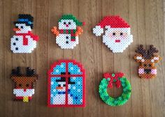 cross stitch christmas ornaments laid out on a wooden table with santa clause, snowman, reindeer, and wreath