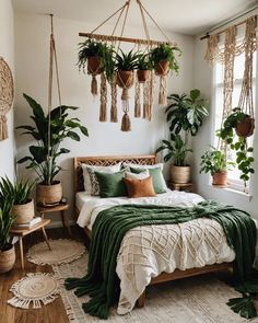 a bedroom with plants hanging from the ceiling and a bed covered in green blankets, pillows and throws