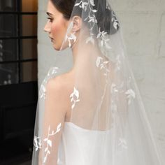 a woman wearing a wedding veil with white flowers on the back of her head and shoulder