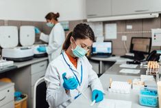 two women in white lab coats and masks working on laboratory equipment at desks with blue liquid