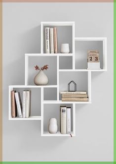 a white shelf filled with books and vases on top of each other next to a green wall