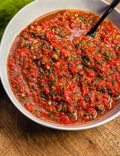 a white bowl filled with lots of red sauce next to a green vegetable on top of a wooden table