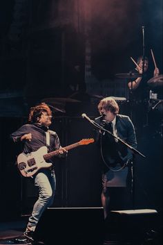 two young men are playing guitars on stage